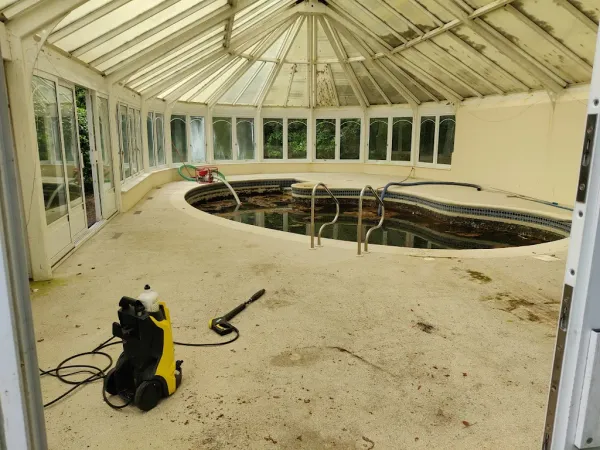 Disused indoor swimming pool full of foul water, pressure washer set up to empty and clean it