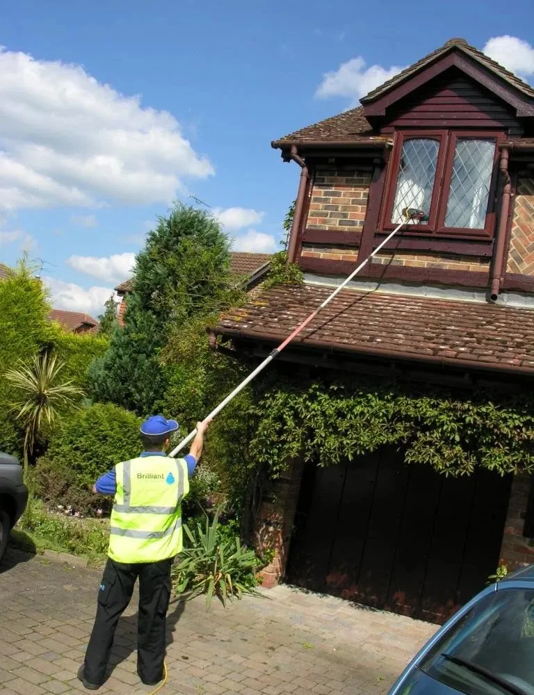 Window cleaner reaching upstairs leaded windows with a pure water pole from the drive, as on our Woking rounds